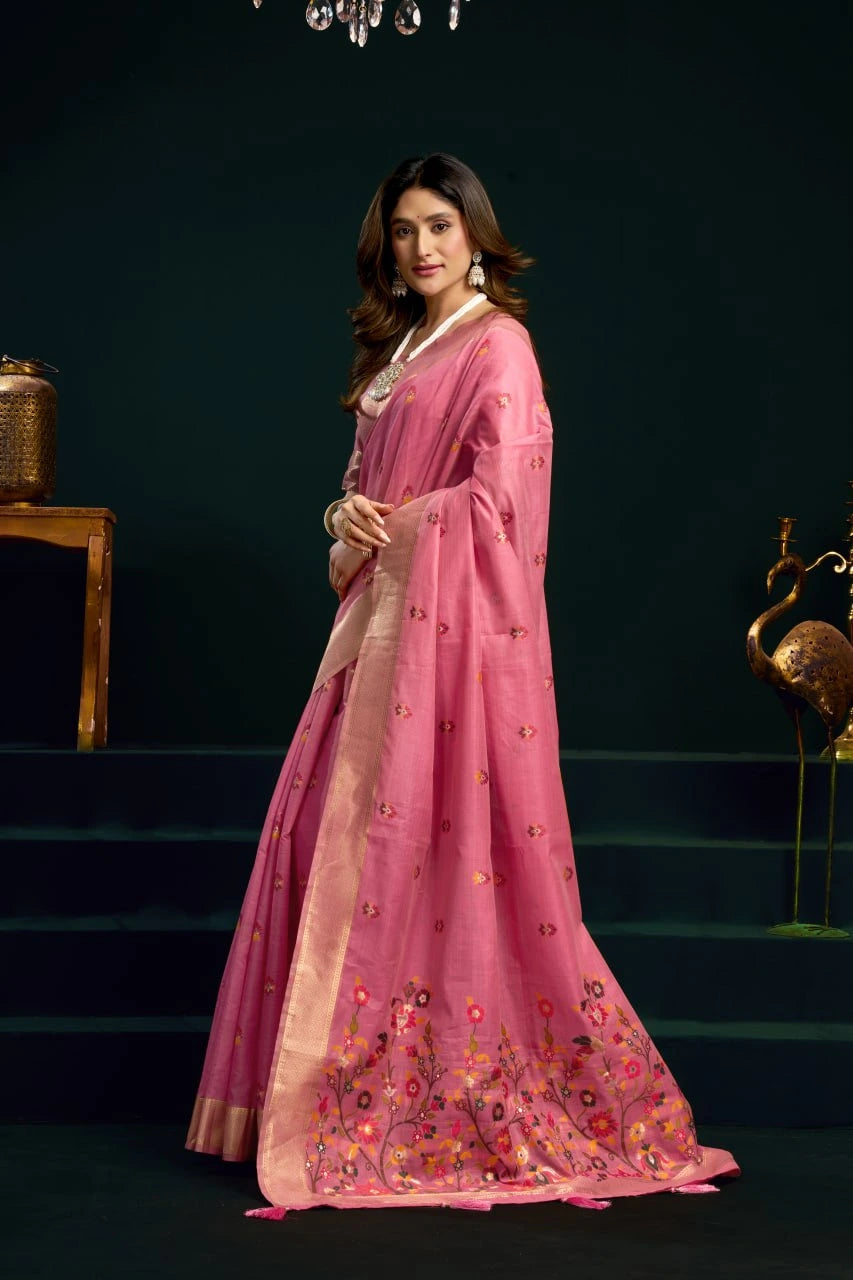Woman in a pink traditional outfit with floral embroidery standing against a dark background.